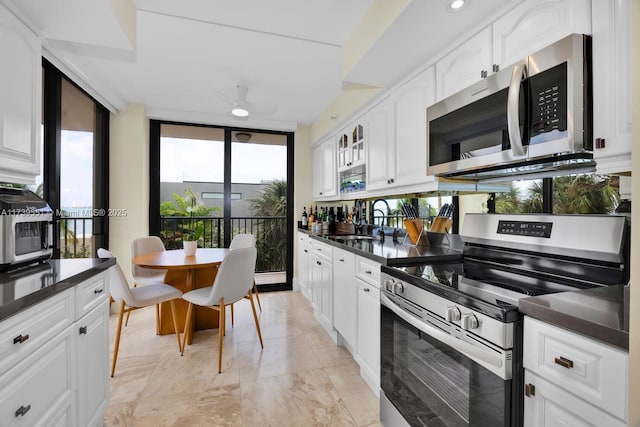 kitchen with dark countertops, appliances with stainless steel finishes, white cabinets, a sink, and a wall of windows