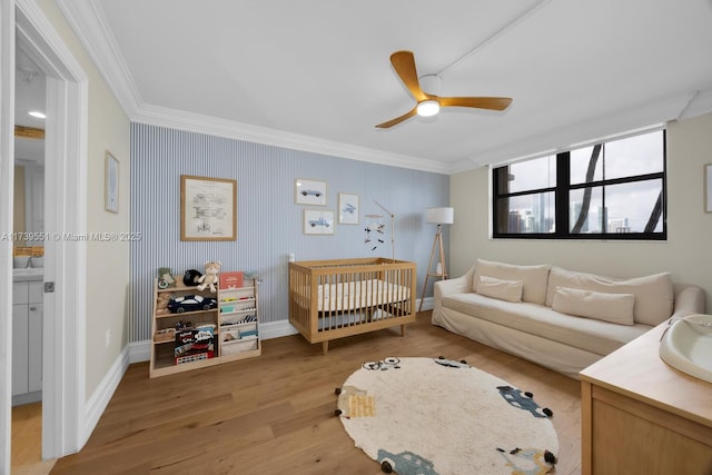 bedroom featuring ceiling fan, baseboards, ornamental molding, a nursery area, and light wood finished floors