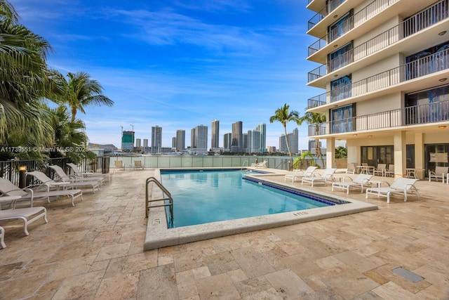 community pool with a patio area, a view of city, and fence