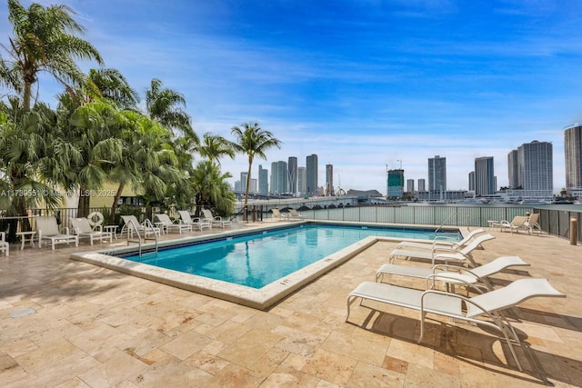 community pool with a view of city, a patio, and fence