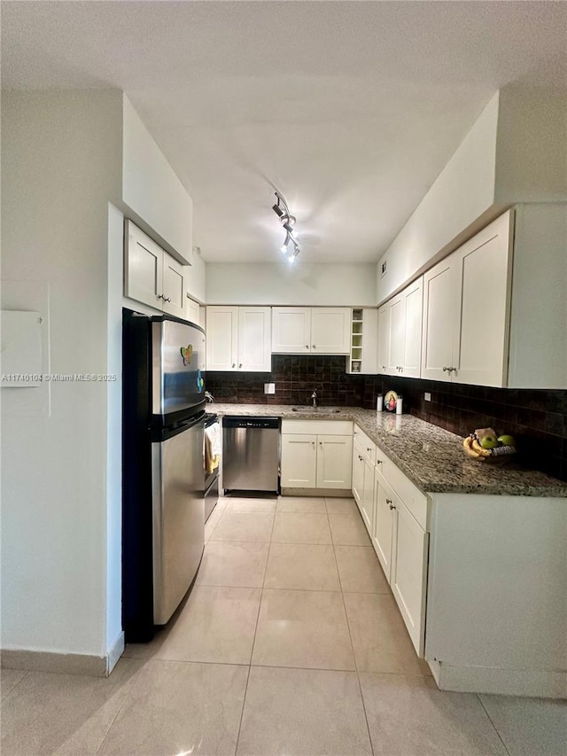 kitchen featuring appliances with stainless steel finishes, white cabinets, decorative backsplash, dark stone counters, and light tile patterned floors