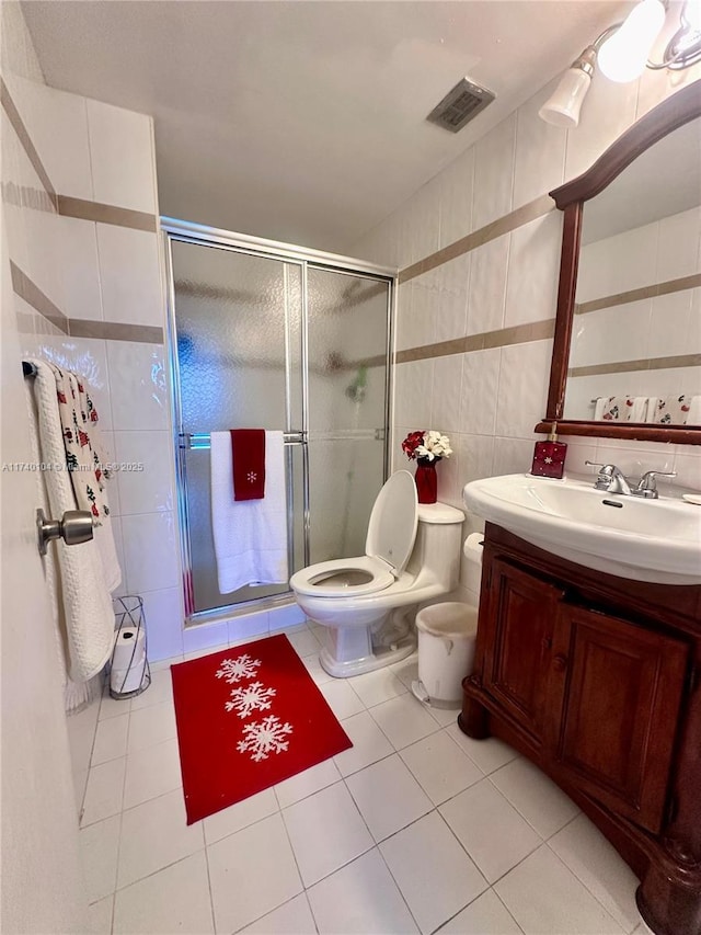 bathroom with tile walls, tile patterned flooring, vanity, toilet, and a shower with door