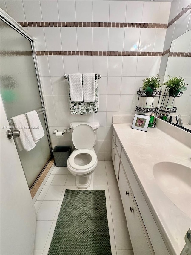 bathroom with a shower with door, tile walls, vanity, tile patterned floors, and toilet