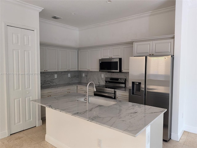 kitchen with ornamental molding, appliances with stainless steel finishes, a center island with sink, and light stone counters