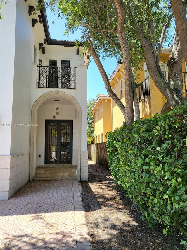 property entrance featuring a balcony, french doors, fence, and stucco siding