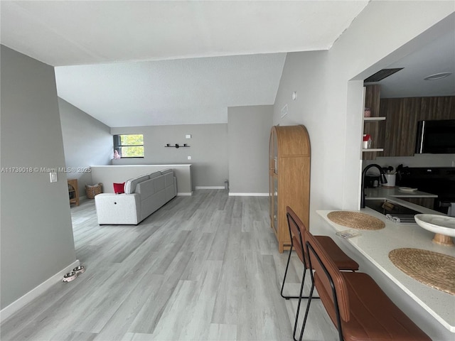 living room featuring vaulted ceiling, sink, and light hardwood / wood-style flooring