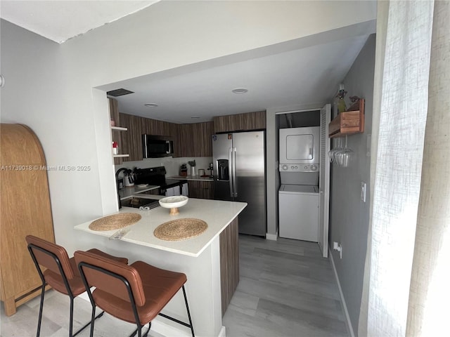 kitchen featuring stainless steel fridge with ice dispenser, kitchen peninsula, a breakfast bar area, stacked washer and dryer, and black range with electric cooktop