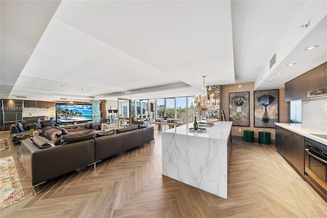 living room with a notable chandelier, a raised ceiling, and light parquet floors