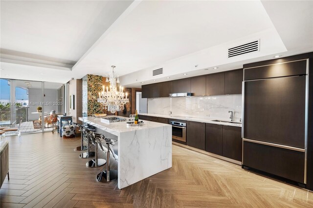 kitchen featuring sink, stainless steel oven, light parquet floors, and a center island with sink