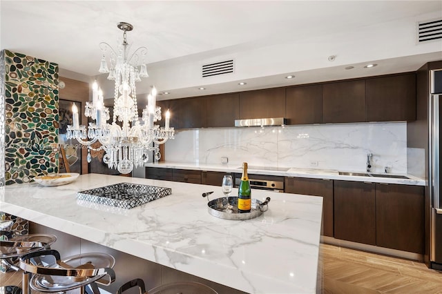 kitchen with dark brown cabinetry, sink, a breakfast bar area, pendant lighting, and backsplash