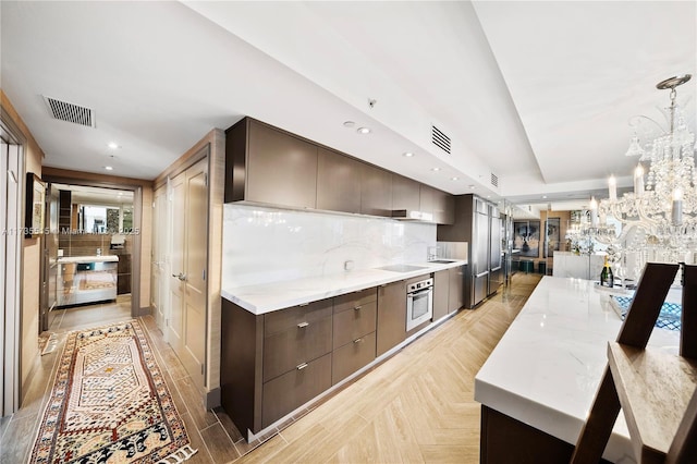 kitchen with light parquet floors, backsplash, hanging light fixtures, light stone countertops, and stainless steel oven