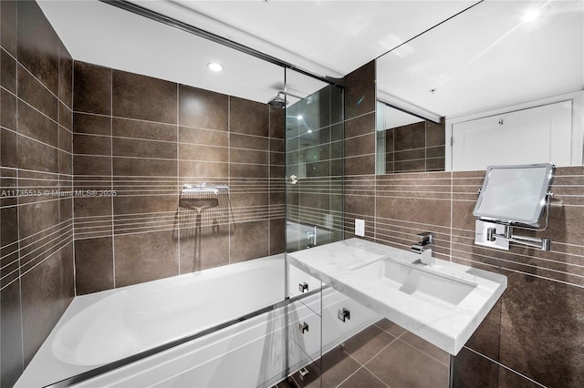 bathroom featuring combined bath / shower with glass door, sink, tile walls, and backsplash