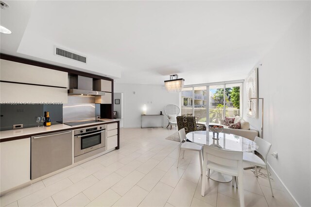 kitchen with appliances with stainless steel finishes, white cabinets, hanging light fixtures, a notable chandelier, and wall chimney range hood