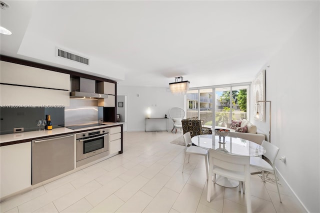 kitchen featuring white cabinetry, appliances with stainless steel finishes, a notable chandelier, pendant lighting, and wall chimney range hood