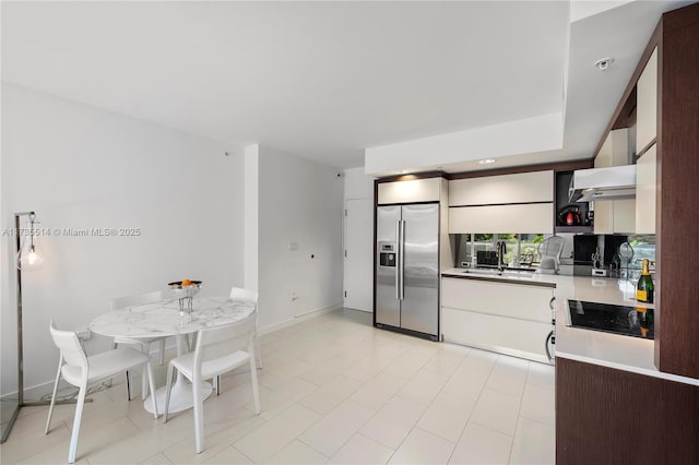 kitchen featuring black electric stovetop, sink, wall chimney exhaust hood, and stainless steel built in fridge