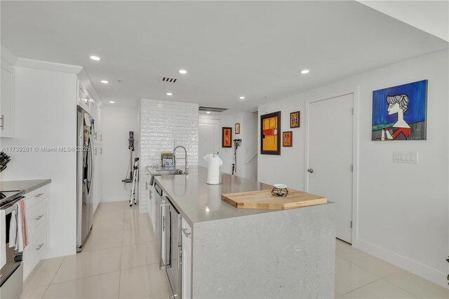 kitchen with light tile patterned flooring, sink, white cabinetry, appliances with stainless steel finishes, and an island with sink