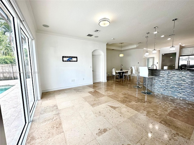 kitchen featuring pendant lighting, stainless steel refrigerator with ice dispenser, a tray ceiling, ornamental molding, and a textured ceiling