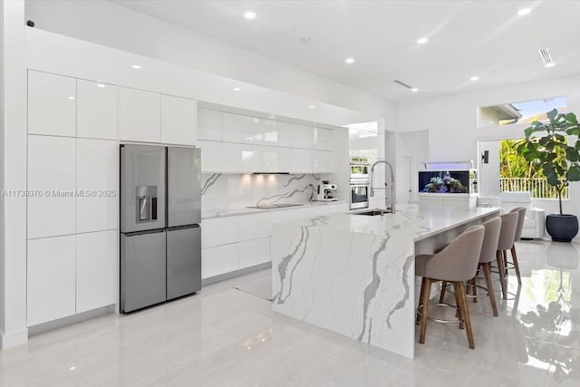 kitchen with a breakfast bar, sink, white cabinetry, a large island with sink, and stainless steel appliances