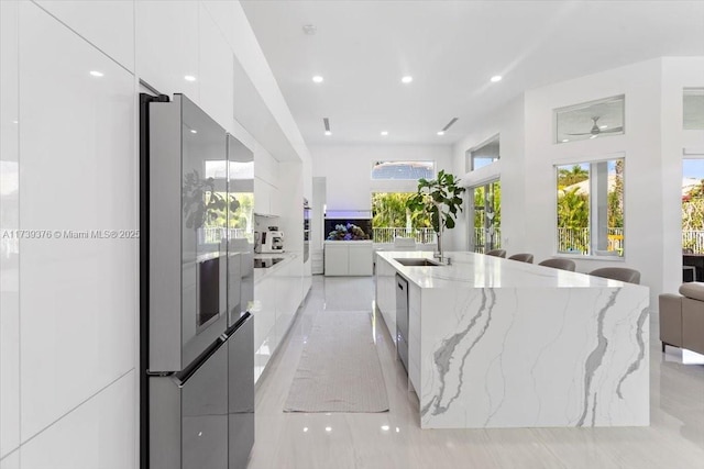 kitchen with sink, appliances with stainless steel finishes, white cabinetry, light stone countertops, and a large island with sink