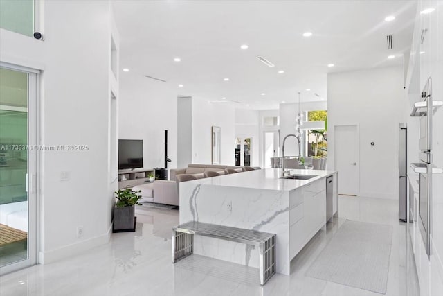 kitchen with white cabinetry, an island with sink, sink, hanging light fixtures, and light stone countertops