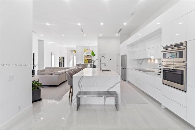 kitchen featuring a kitchen bar, sink, a center island with sink, stainless steel double oven, and white cabinets