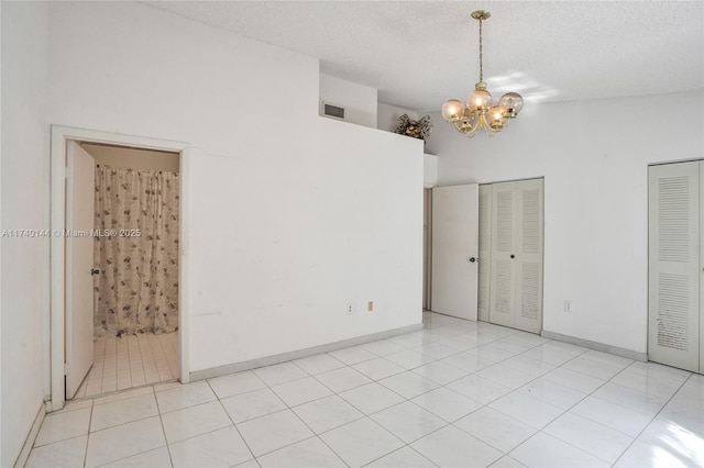 unfurnished bedroom with light tile patterned flooring, lofted ceiling, an inviting chandelier, a textured ceiling, and two closets