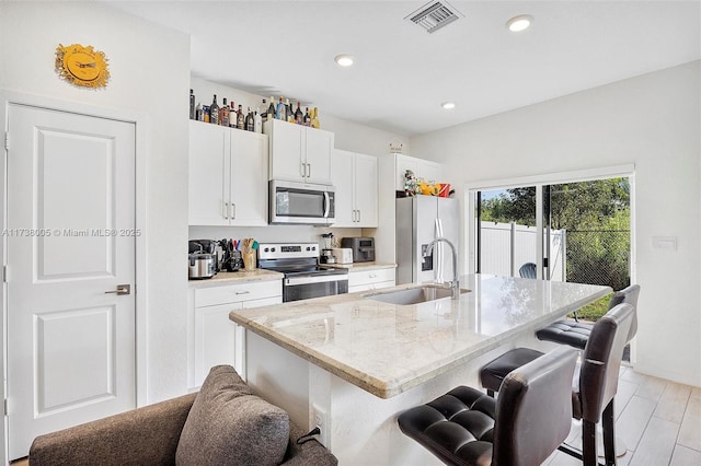 kitchen with sink, a kitchen island with sink, white cabinetry, stainless steel appliances, and a kitchen bar