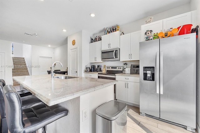 kitchen featuring white cabinetry, stainless steel appliances, a kitchen bar, and an island with sink