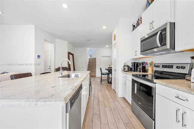 kitchen with sink, stainless steel appliances, light stone countertops, a kitchen island with sink, and white cabinets