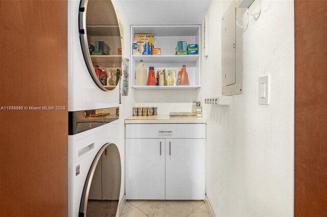 washroom featuring cabinets, stacked washer and dryer, electric panel, and light tile patterned flooring