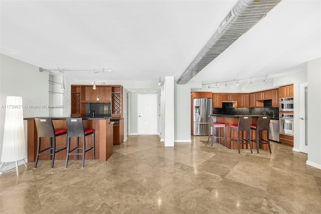 kitchen with appliances with stainless steel finishes, track lighting, a kitchen bar, and decorative backsplash