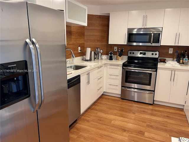 kitchen featuring appliances with stainless steel finishes, wood walls, white cabinetry, sink, and light hardwood / wood-style flooring