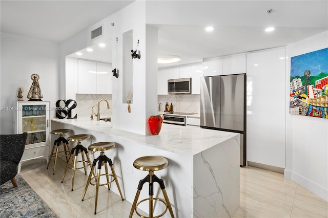 kitchen with a breakfast bar, appliances with stainless steel finishes, kitchen peninsula, and white cabinets