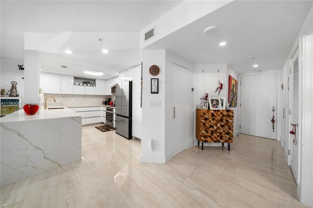 kitchen with sink, light stone counters, kitchen peninsula, stainless steel appliances, and white cabinets