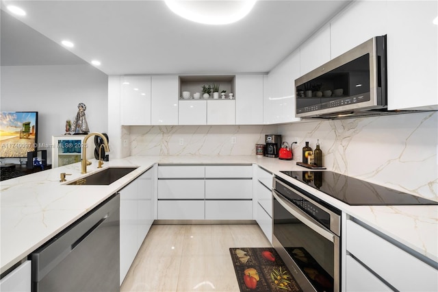 kitchen featuring appliances with stainless steel finishes, white cabinetry, sink, backsplash, and light stone countertops