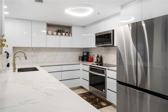 kitchen with white cabinetry, sink, backsplash, stainless steel appliances, and light stone countertops