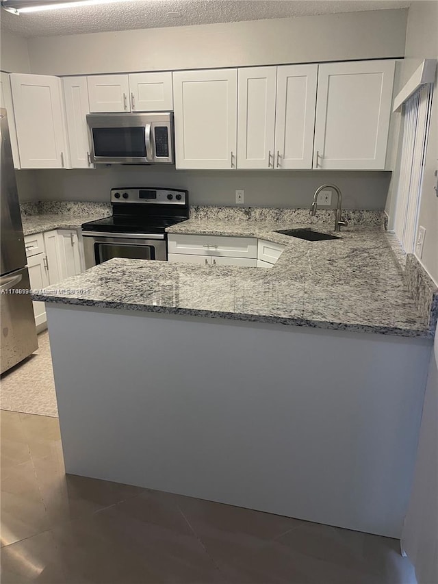 kitchen featuring appliances with stainless steel finishes, white cabinetry, sink, light stone counters, and a textured ceiling