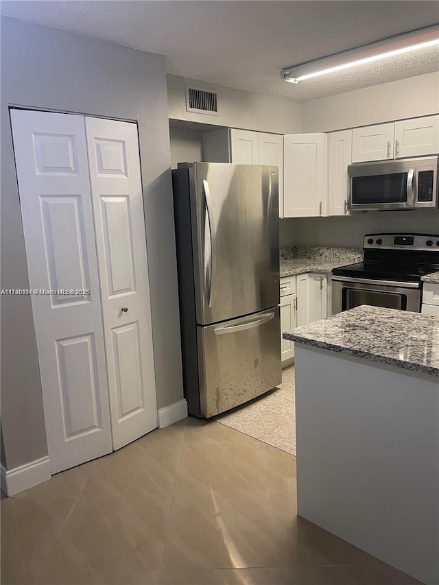 kitchen with light tile patterned floors, appliances with stainless steel finishes, white cabinetry, light stone counters, and a textured ceiling