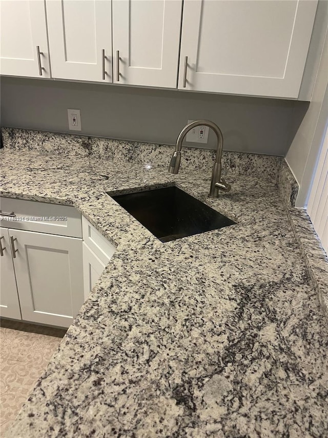 kitchen with light stone counters, sink, and white cabinets