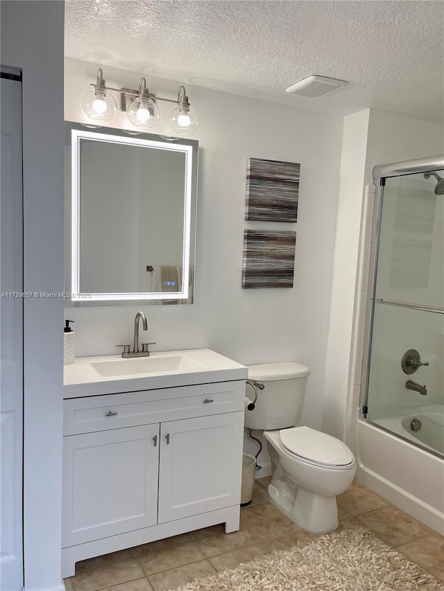 full bathroom featuring tile patterned flooring, bath / shower combo with glass door, vanity, a textured ceiling, and toilet