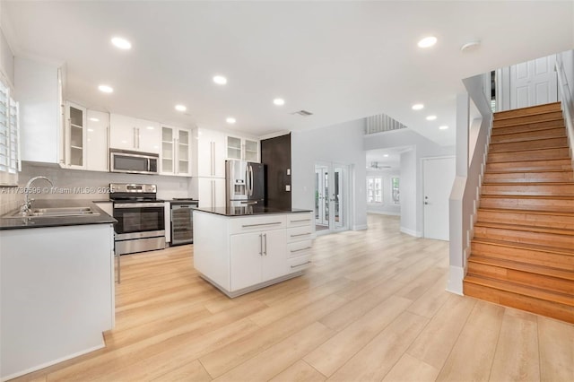 kitchen with sink, a center island, light wood-type flooring, stainless steel appliances, and white cabinets