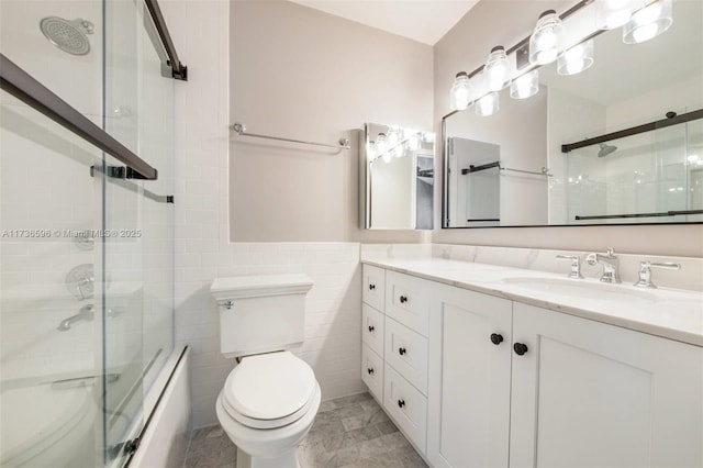 full bathroom with vanity, bath / shower combo with glass door, tile walls, and toilet