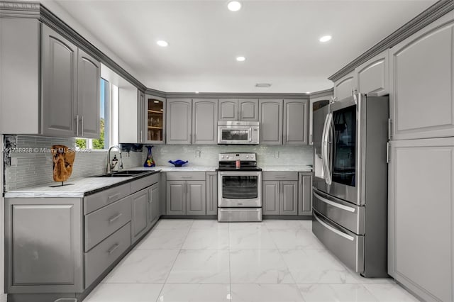 kitchen featuring stainless steel appliances, gray cabinets, a sink, and marble finish floor