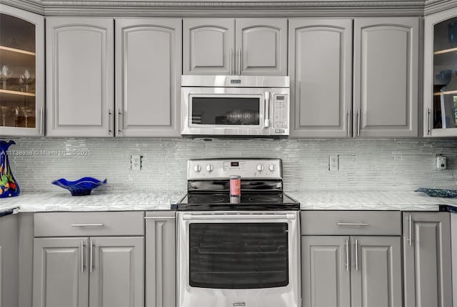 kitchen featuring tasteful backsplash, light countertops, gray cabinetry, appliances with stainless steel finishes, and glass insert cabinets