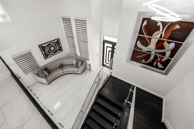 living area featuring a towering ceiling, marble finish floor, and baseboards