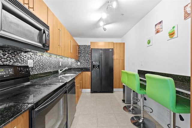 kitchen featuring light tile patterned flooring, a sink, decorative backsplash, black appliances, and dark stone countertops