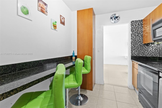 kitchen featuring light tile patterned floors, black appliances, brown cabinetry, and decorative backsplash