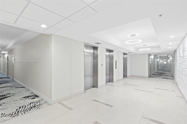 hall with elevator, baseboards, a raised ceiling, and recessed lighting