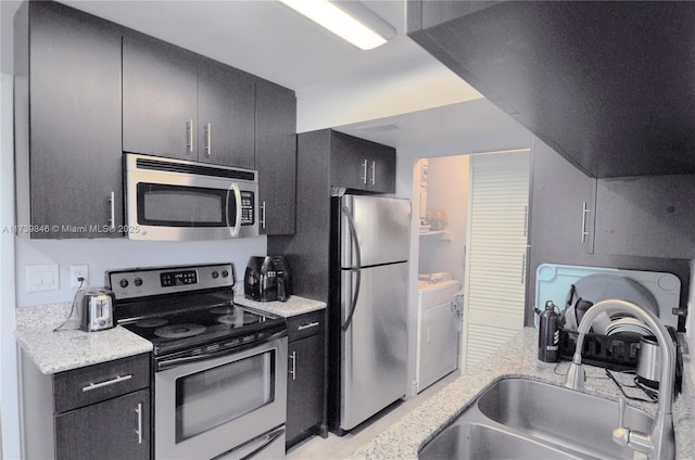 kitchen with washer / clothes dryer, sink, stainless steel appliances, and light stone countertops