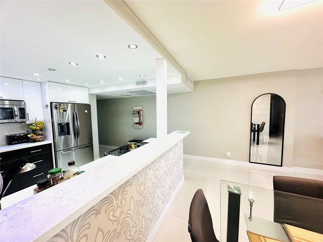 kitchen featuring light tile patterned floors, stainless steel appliances, white cabinets, and light stone countertops